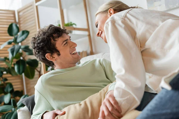 Happy young couple smiling while having pillow fight in living room — Fotografia de Stock