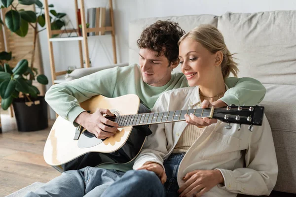 Curly man playing acoustic guitar near cheerful blonde woman — Photo de stock