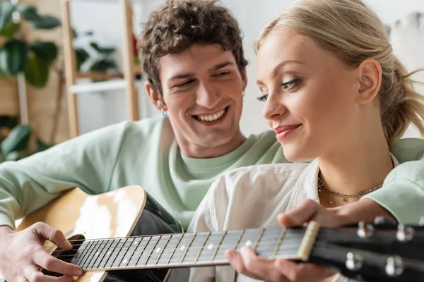 Happy man playing acoustic guitar near blonde woman on blurred foreground — Stock Photo