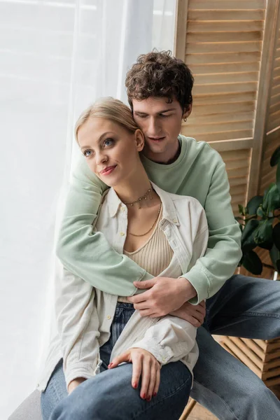 Curly man hugging young blonde girlfriend in shirt and jeans — Stock Photo