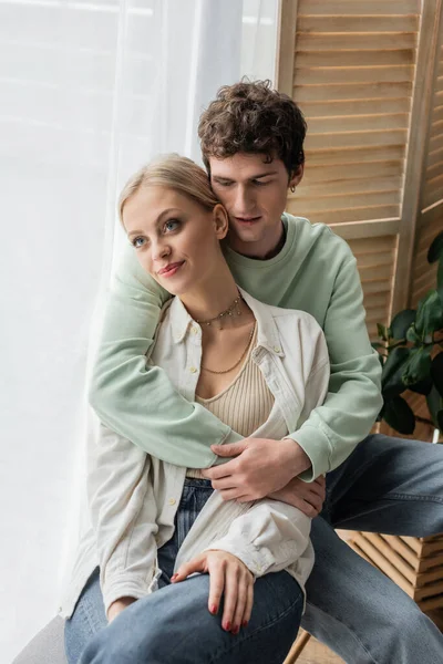 Curly man hugging young blonde girlfriend in shirt and jeans — стоковое фото