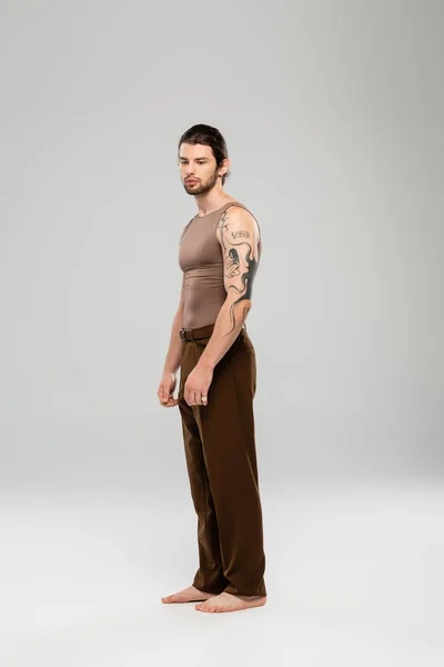 Full length of barefoot tattooed man standing on grey background — Stock Photo