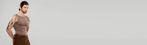 Бородатий і татуйований молодий чоловік дивиться ізольовано на сірий, банер — стокове фото