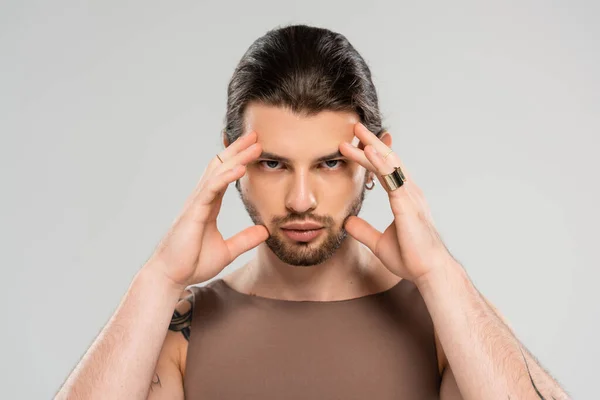 Portrait of brunette and tattooed man touching face isolated on grey — Stock Photo