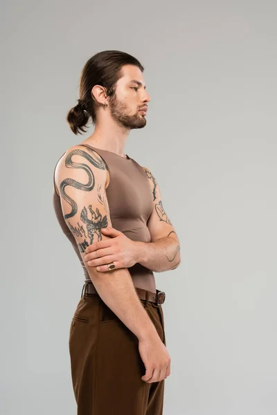 Side view of young tattooed man in brown tank top standing isolated on grey - foto de stock