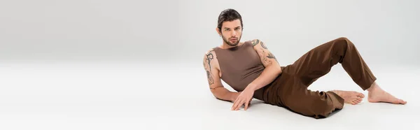 Young tattooed man posing while lying on grey background, banner — Stock Photo