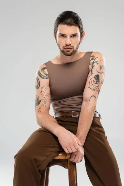Stylish and tattooed man sitting on chair isolated on grey — Stockfoto