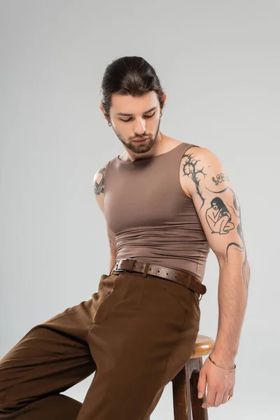 Stylish tattooed man in brown tank top sitting on chair isolated on grey — Stockfoto