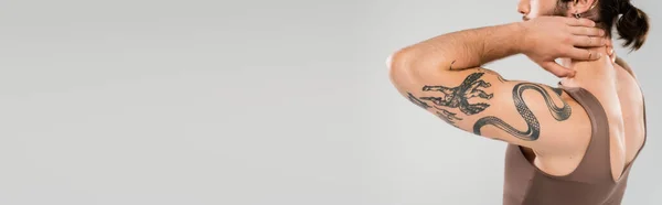 Cropped view of muscular man in tank top touching neck isolated on grey, banner - foto de stock