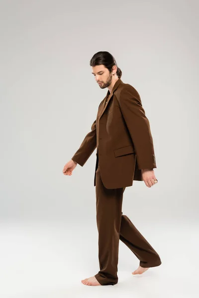 Full length of stylish long haired man in suit walking on grey background — Stock Photo