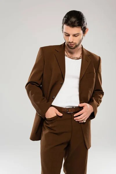Trendy young man posing in brown suit isolated on grey — Stock Photo