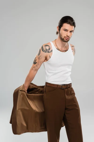 Tattooed man in sleeveless shirt holding jacket isolated on grey — Stockfoto