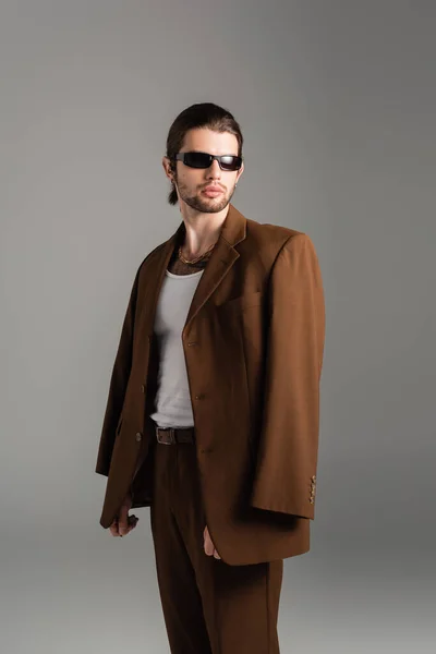 Fashionable man in sunglasses posing in brown suit isolated on grey — Foto stock