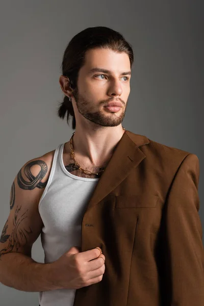 Portrait of tattooed young man in tank top holding jacket isolated on grey — Stockfoto