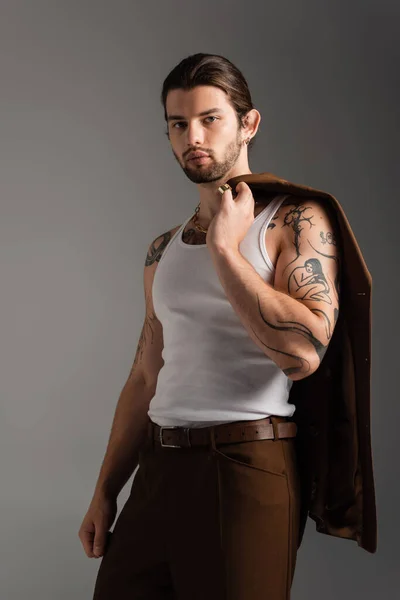Long haired tattooed man holding brown blazer isolated on grey — Stockfoto