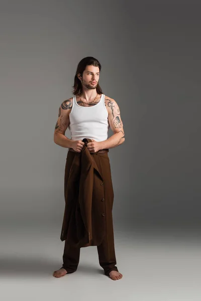 Full length of barefoot and tattooed model holding jacket on grey background — Fotografia de Stock