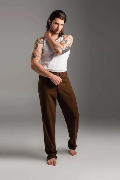 Full length of barefoot and stylish model with tattoo on body posing on grey — стоковое фото