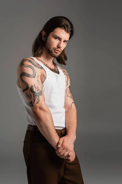 Stylish tattooed man in white sleeveless short looking at camera isolated on grey — Stockfoto
