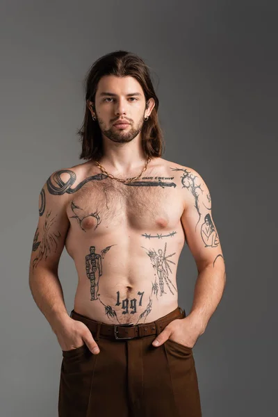 Long haired and tattooed man in pants posing isolated on grey — Photo de stock
