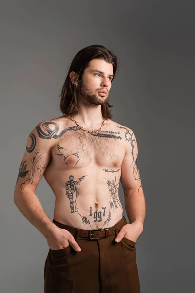 Muscular and tattooed man holding hands in pockets of pants isolated on grey — Photo de stock