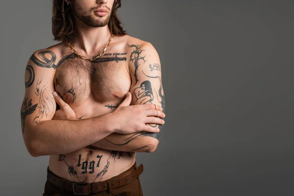 Cropped view of long haired and tattooed man crossing arms isolated on grey - foto de stock