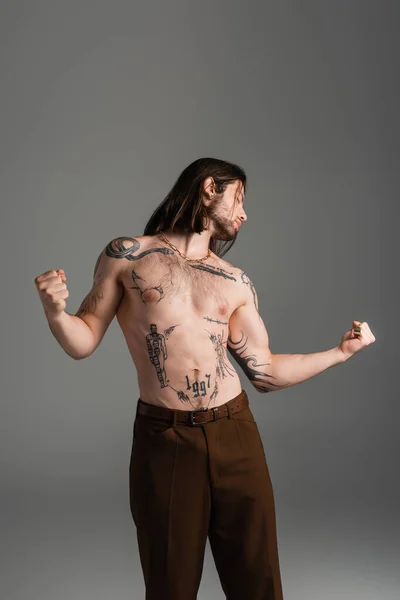 Side view of shirtless tattooed man holding hands in fists isolated on grey — стоковое фото