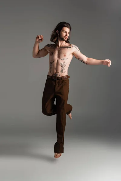 Shirtless and tattooed man jumping on grey background — Stock Photo