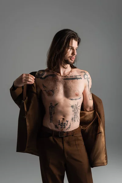 Stylish tattooed man wearing blazer isolated on grey — стоковое фото