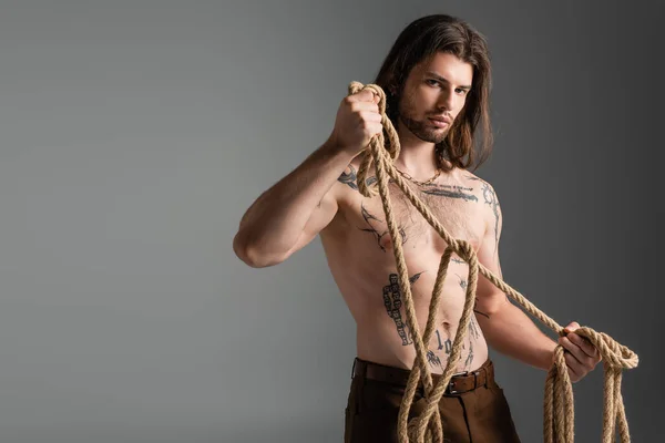 Young long haired model with tattoo on body holding rope isolated on grey — Stockfoto