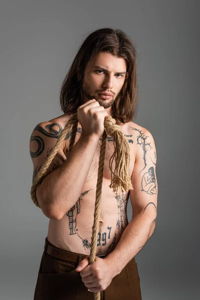 Shirtless tattooed man holding rope and looking at camera isolated on grey — Photo de stock