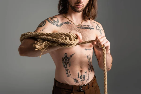 Cropped view of long haired model with tattoo on body holding rope isolated on grey — Foto stock