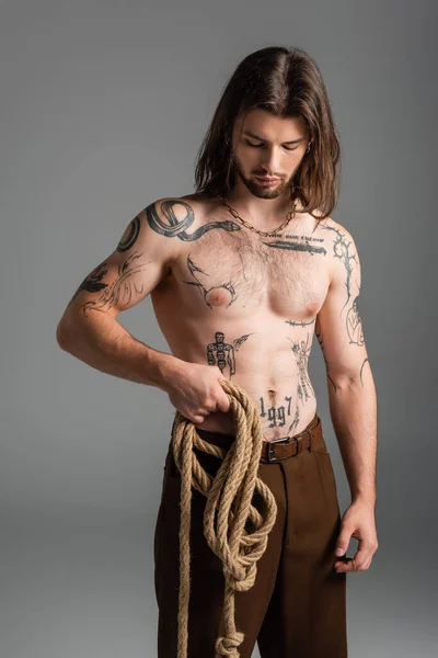 Long haired and tattooed model holding rope isolated on grey — Photo de stock