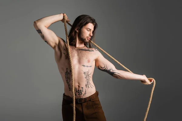 Muscular and tattooed man holding rope isolated on grey - foto de stock