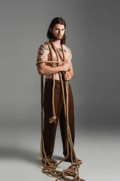 Full length of tattooed man with rope on body on grey background — Stock Photo