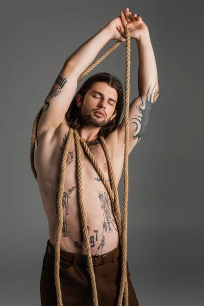 Muscular tattooed model posing with rope isolated on grey — Stock Photo
