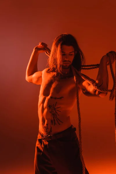 Sexy tattooed model holding rope isolated on red with light — Photo de stock