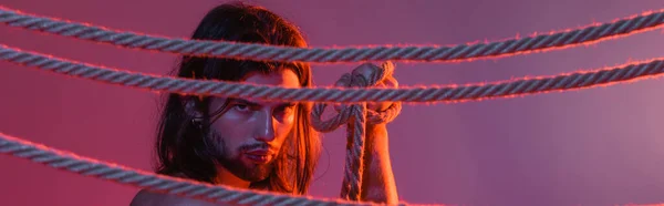 Long haired man holding rope on purple background with light, banner — Stock Photo