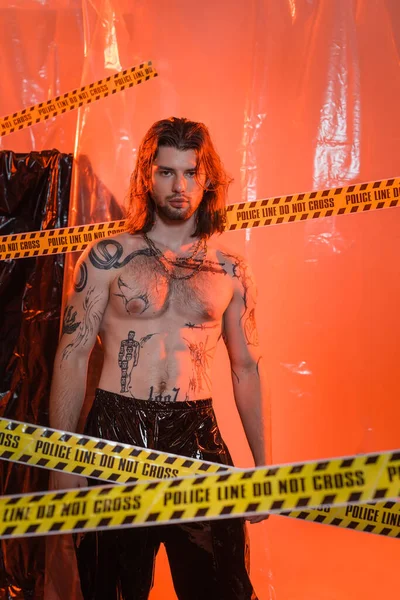 Shirtless tattooed man standing near police line and cellophane - foto de stock