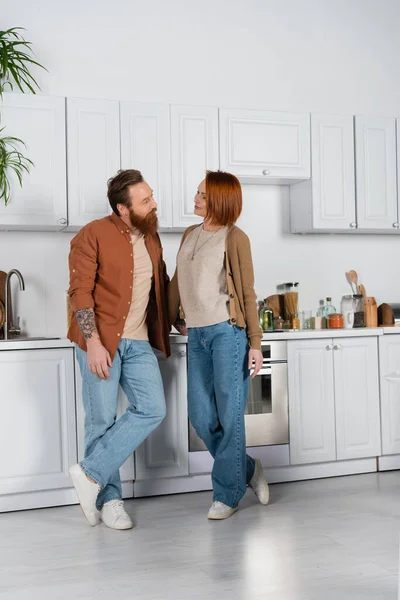 Smiling redhead woman looking at husband in kitchen — Foto stock