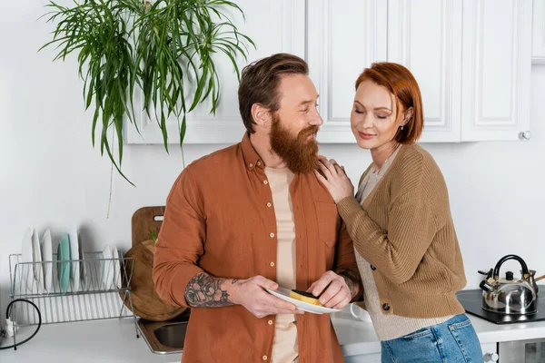 Redhead woman hugging husband washing plate in kitchen — Stock Photo