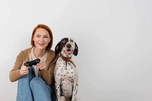KYIV, UKRAINE - DECEMBER 16, 2022: Smiling red haired woman playing video game near dalmatian dog — Photo de stock