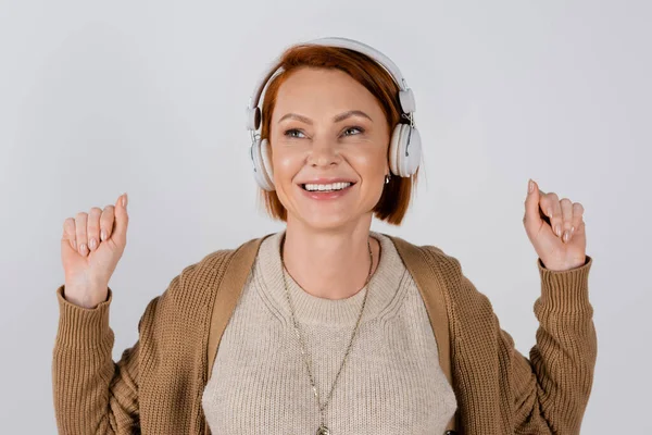 Positive red haired woman in headphones and casual clothes isolated on grey — Stock Photo