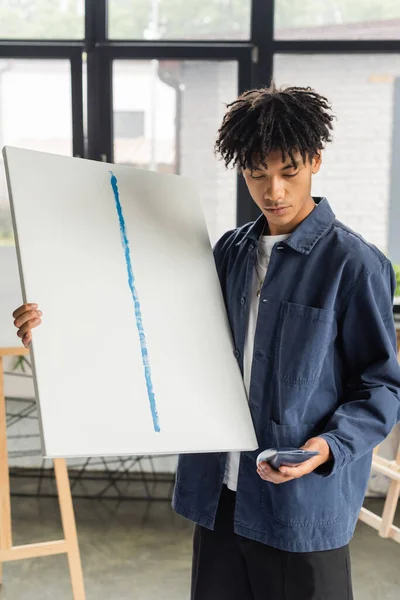 Молодий афроамериканець, який тримає полотно і малює в студії. — стокове фото
