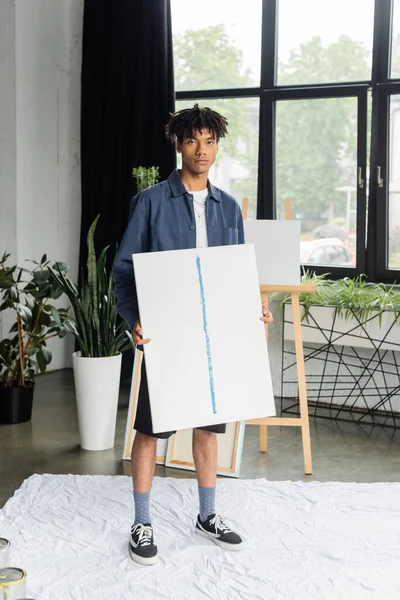 Young african american artist holding painting on cloth in studio — Stock Photo