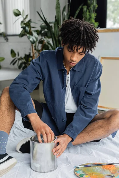 African american artist opening jar with paint near palette in workshop — Stock Photo