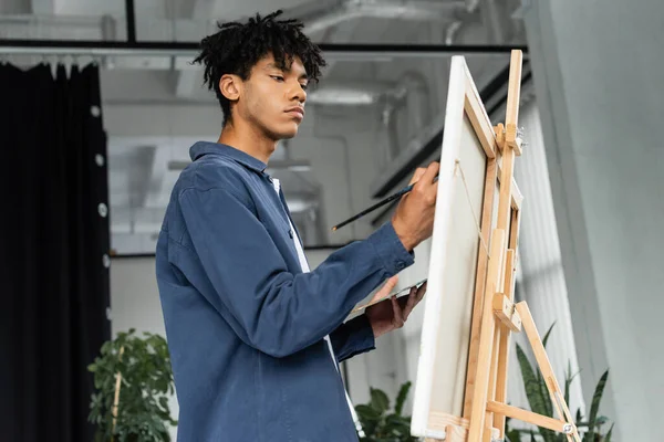 African american artist painting on canvas on easel in studio — Stock Photo
