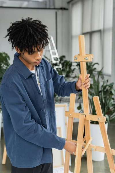 Artista afro-americano ajustando cavalete de madeira em oficina — Fotografia de Stock