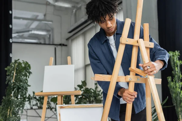 Jovem artista afro-americano regulando cavalete em estúdio — Fotografia de Stock