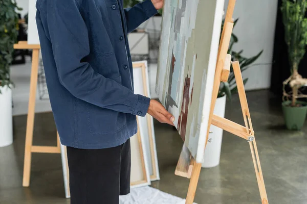 Ausgeschnittene Ansicht eines afrikanisch-amerikanischen Künstlers, der Gemälde von der Staffelei im Atelier nimmt — Stockfoto