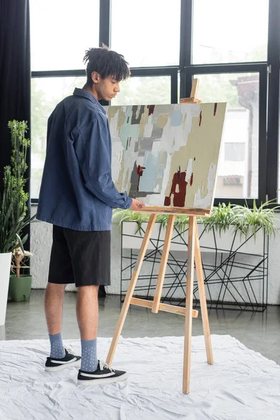 Side view of young african american artist holding painting in workshop — Stock Photo